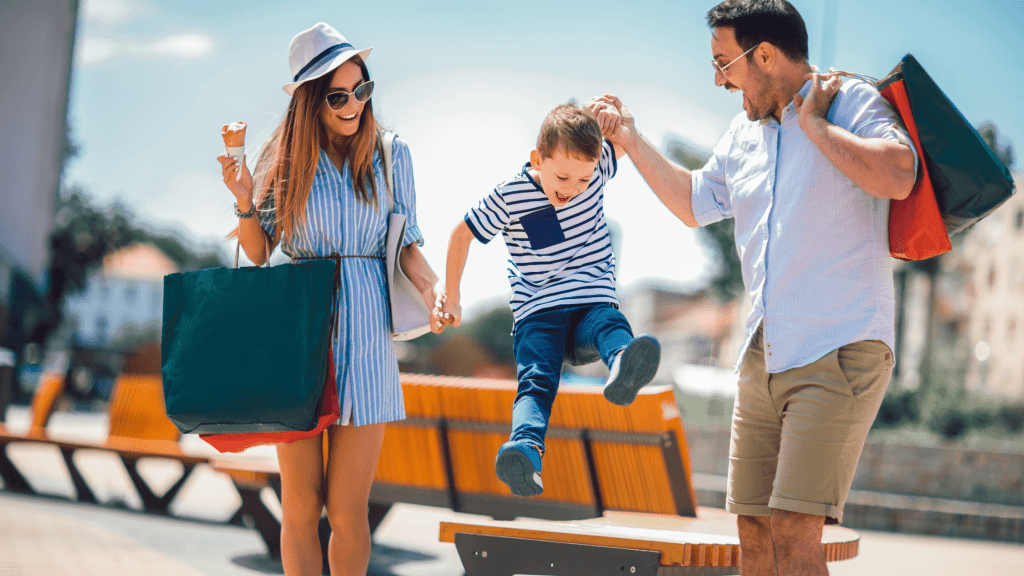 couple and small child smiling jumping off seat holding shopping bags