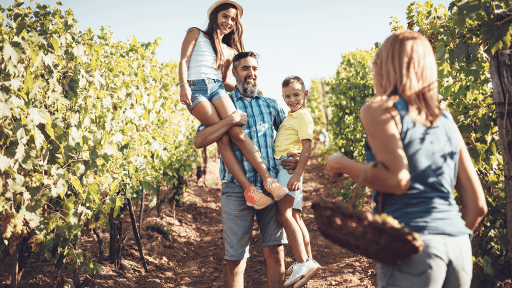 man holding kids in his arm smiling and walking on a farm orchard