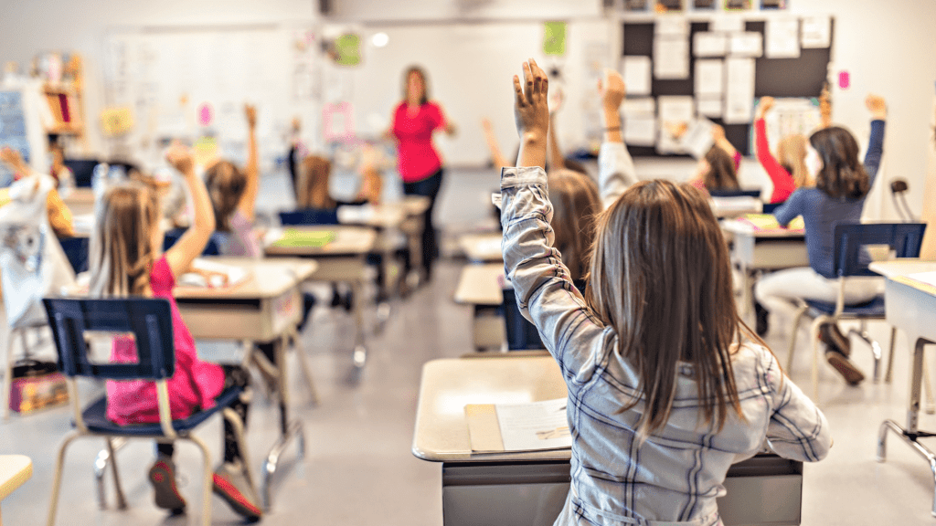 children in a classroom setting with their hands raised