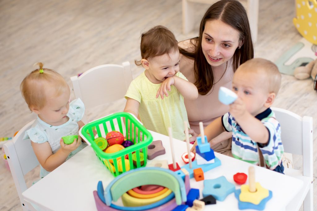 Woman babysitting kids around table playing with toys