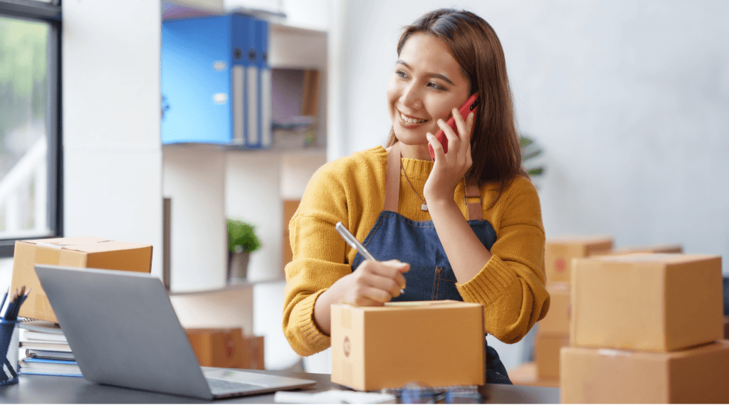 woman smiling holding a phone to her ear while holding pen over a box