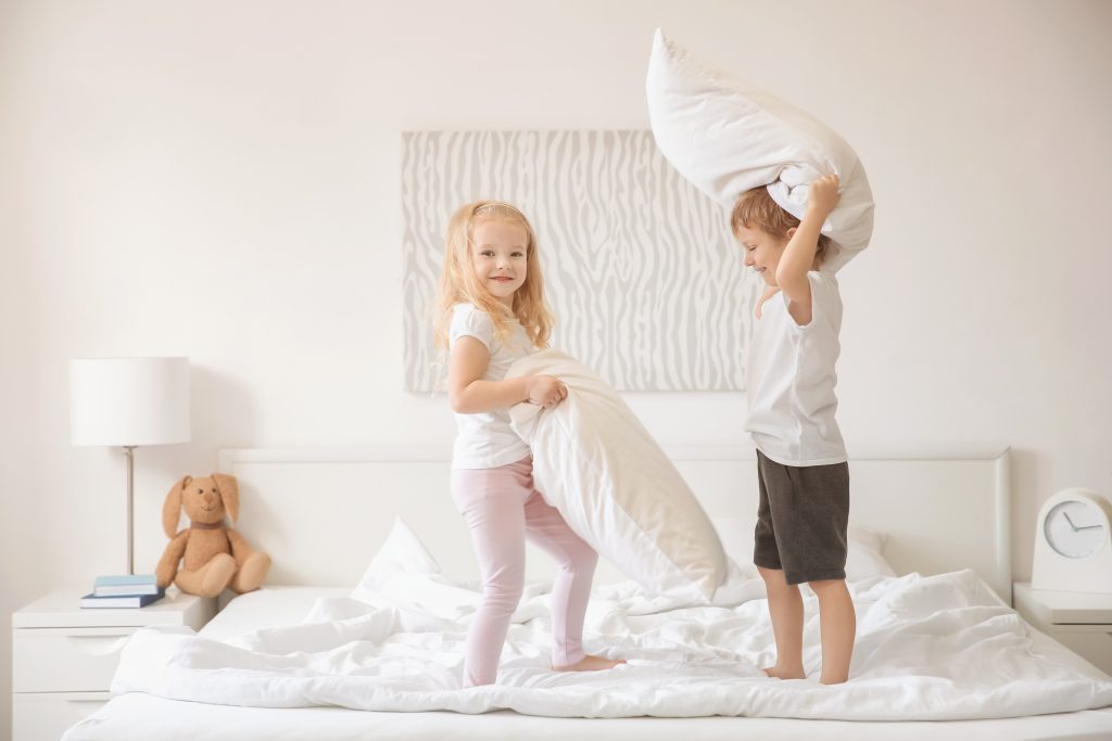 Cute children having fun on bed together playing pillow fight