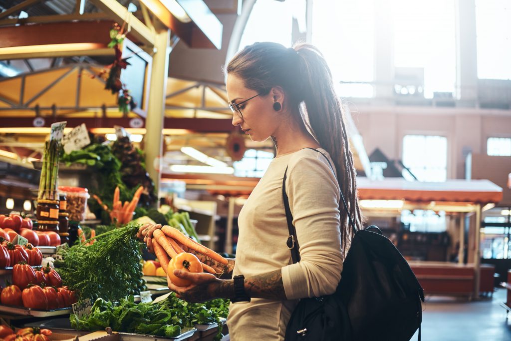 Beautiful pensive girl in glasses is buying fresh carrots at local farmer's market.