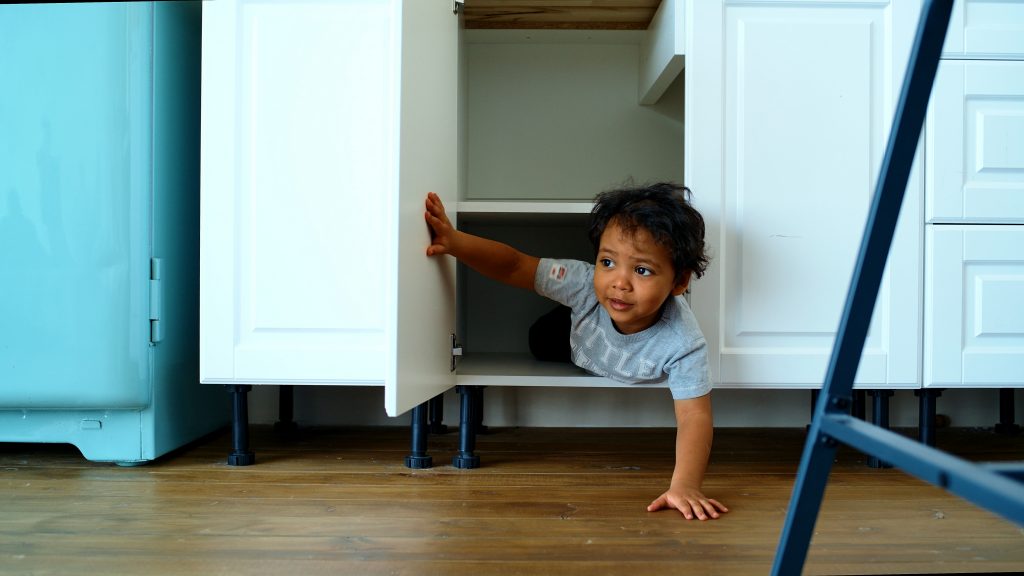 Family at home concept, little boy playing hide and seek. A happy child looks out of the closet in the kitchen.