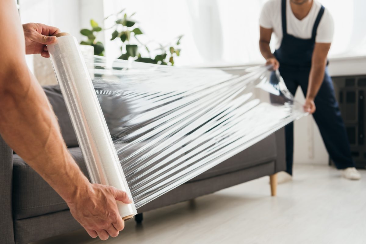 cropped view of movers holding stretch film roll near sofa cropped view of movers holding stretch film roll near sofa