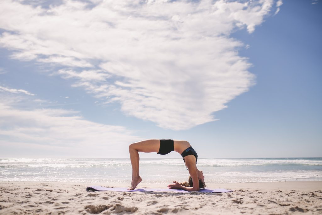Sporty woman doing back bend at the beach. Woman doing stretching workout along the beach.
