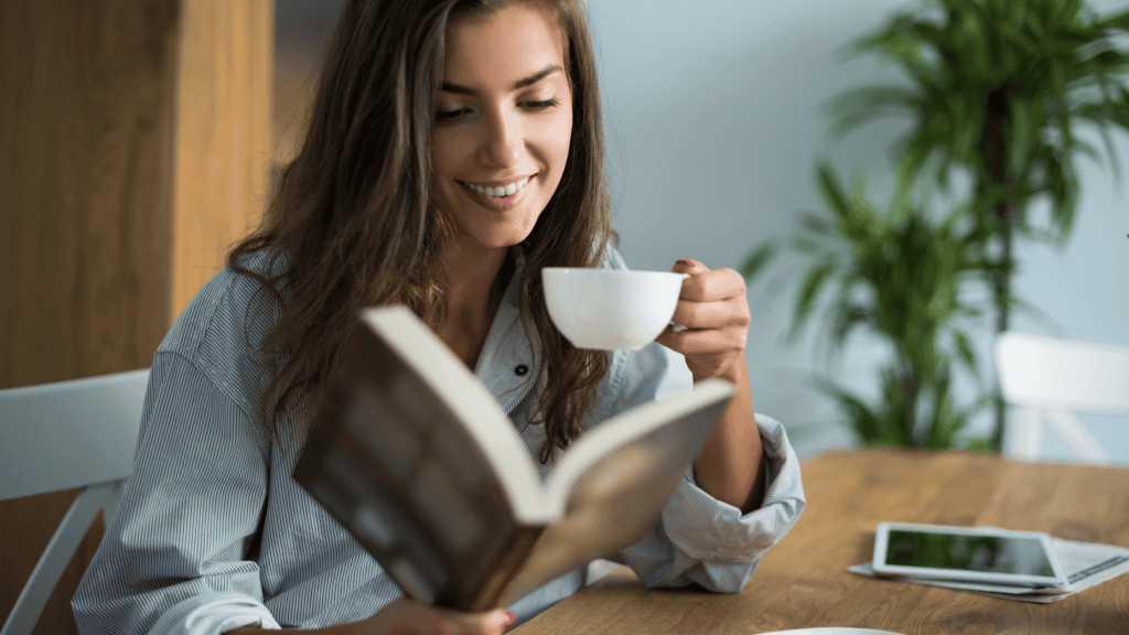 woman smiling holding a mug while reading a book