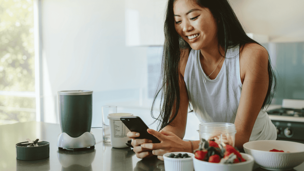 woman smiling looking at cell phone while making breakfast