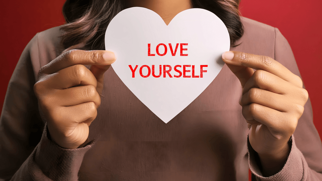 Person holding heart shape cut out of paper with words love yourself imprinted
