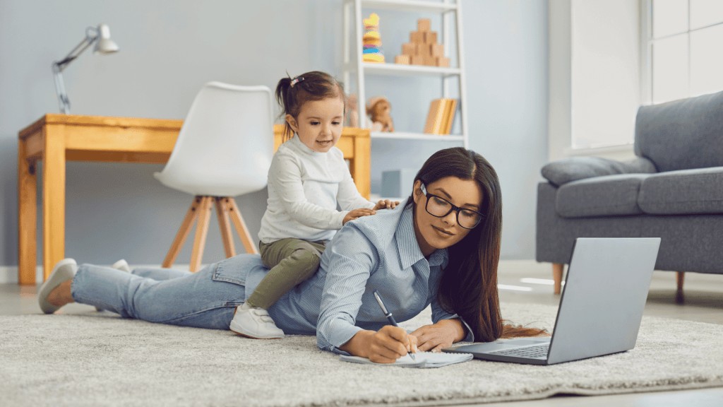 woman on floor with baby on her back while writing multi tasking