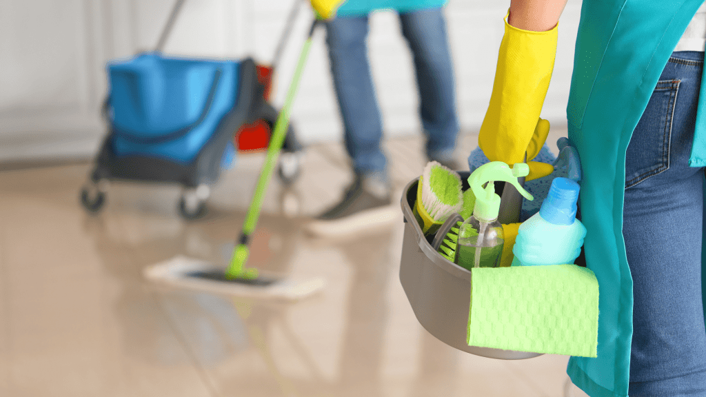 person holding bucket with cleaning supplies while another cleans